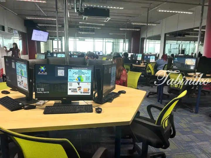 Modern open-plan office with rows of desks, computers, and bright yellow-green chairs in a professional workspace.