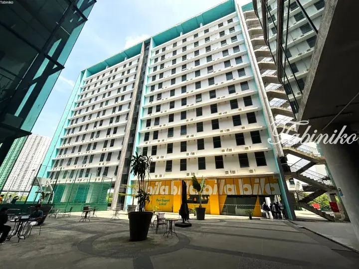 Modern multi-story apartment building with yellow ground-floor signage and a paved courtyard area.