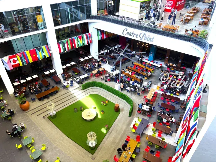 Aerial view of Centre Point shopping mall atrium with international flags, food court seating, and a central green space.