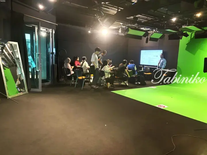 A group attends a presentation in a studio with a green screen and professional lighting equipment.