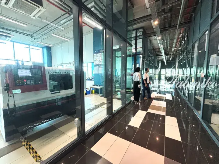 Interior view of a modern industrial facility with glass-walled CNC machining rooms and polished checkered flooring.