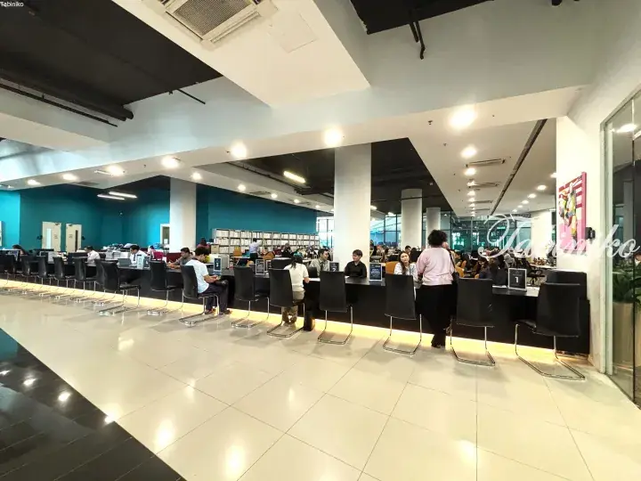Modern library interior with rows of computer workstations and teal walls in a spacious, well-lit study area.