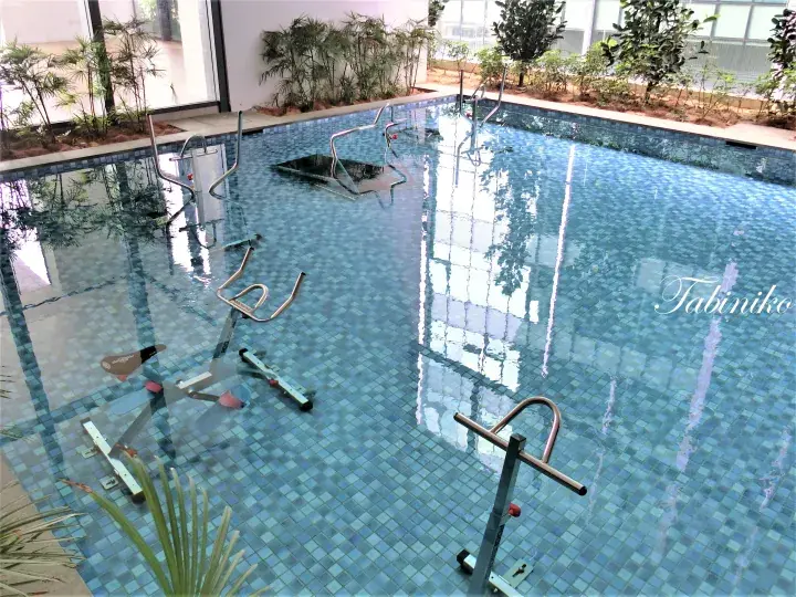 Indoor swimming pool with underwater exercise bikes and glass walls overlooking greenery.