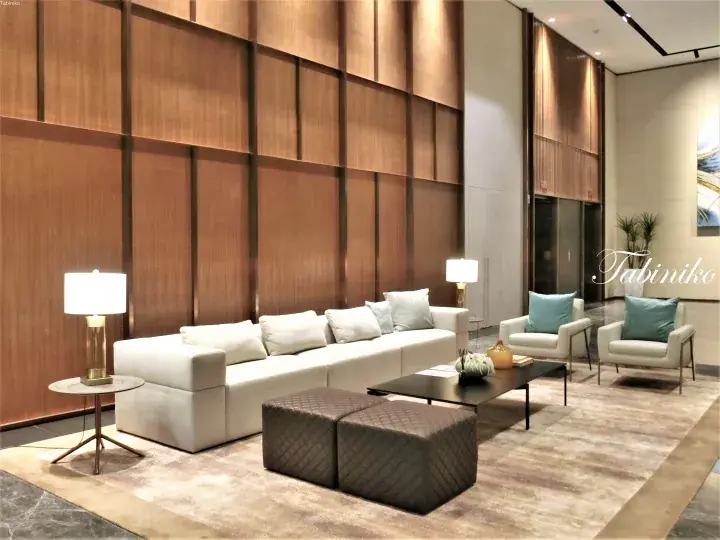 Modern hotel lobby with white sofa, wooden wall panels, and elegant lighting fixtures.
