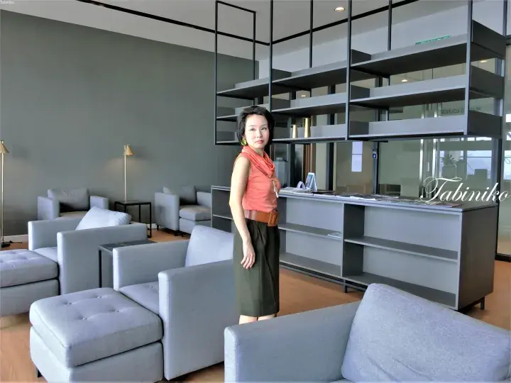 Woman posing in a modern hotel lobby with grey sofas and a stylish shelving unit.
