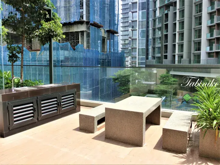 Modern rooftop terrace with stone dining set and outdoor kitchen overlooking a high-rise residential complex in Kuala Lumpur.