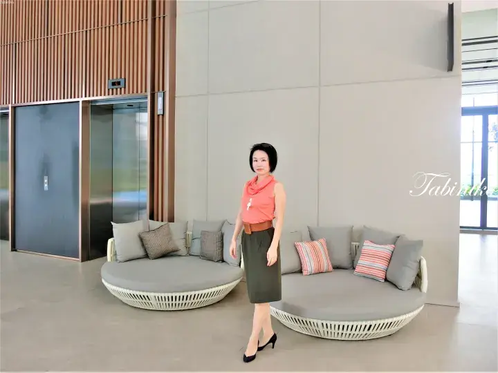 Woman standing in a modern lobby with circular lounge seating and elevator doors.