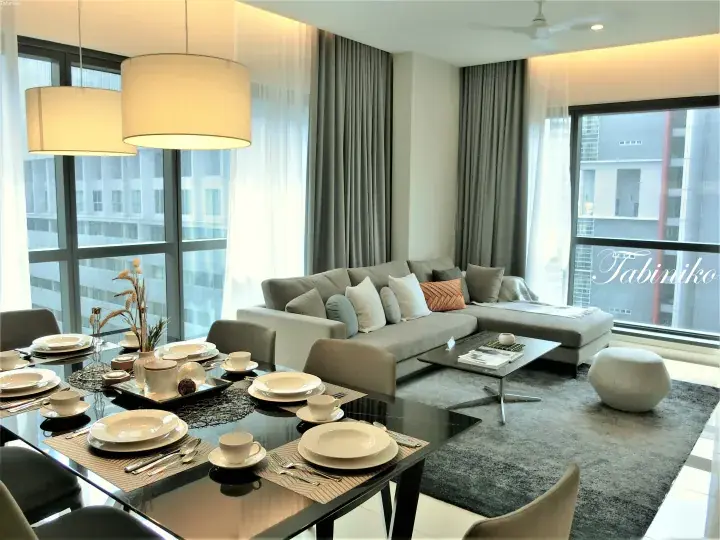 Modern dining table set for four in a bright apartment with a grey sectional sofa and large windows.