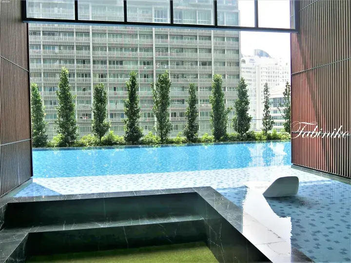 Modern infinity pool with dark marble steps overlooking a row of trees and high-rise buildings in Malaysia.
