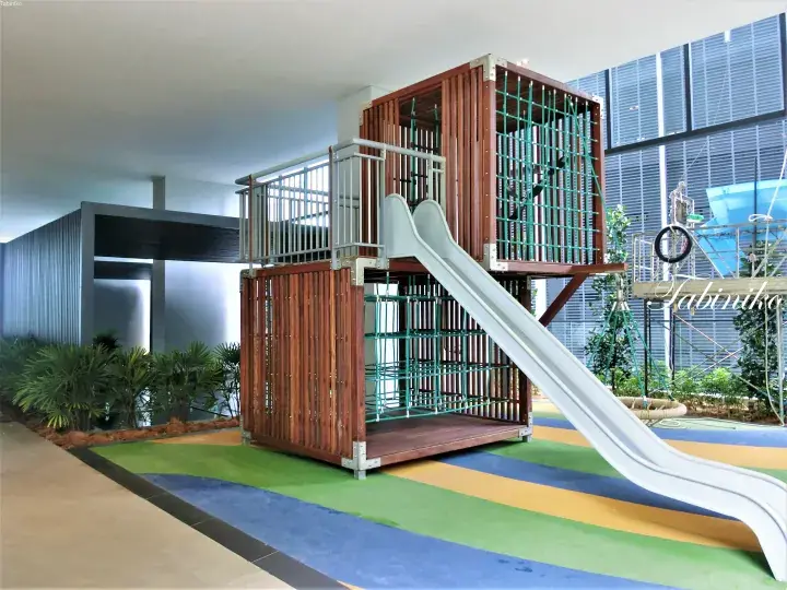 Modern indoor playground featuring a wooden climbing structure with a slide and safety netting in a bright, landscaped area.