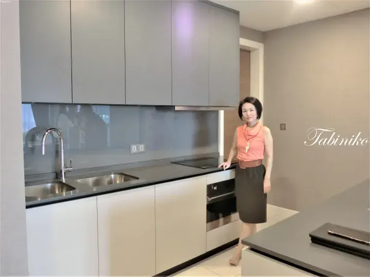 Woman standing in a modern kitchen with grey cabinets, a double sink, and a built-in oven.
