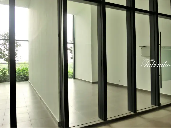 Modern interior with floor-to-ceiling glass walls and black frames, featuring white walls, tiled floors, and lush greenery outside.