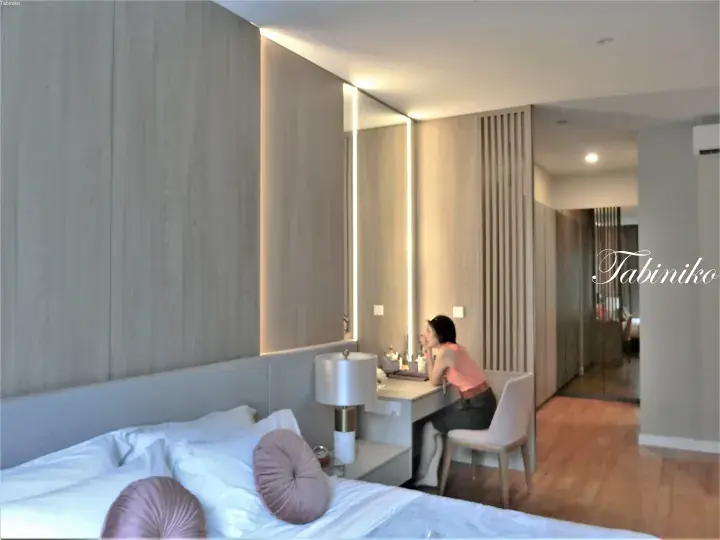 Woman sitting at a modern vanity desk with LED mirror in a contemporary hotel room with wood paneling.