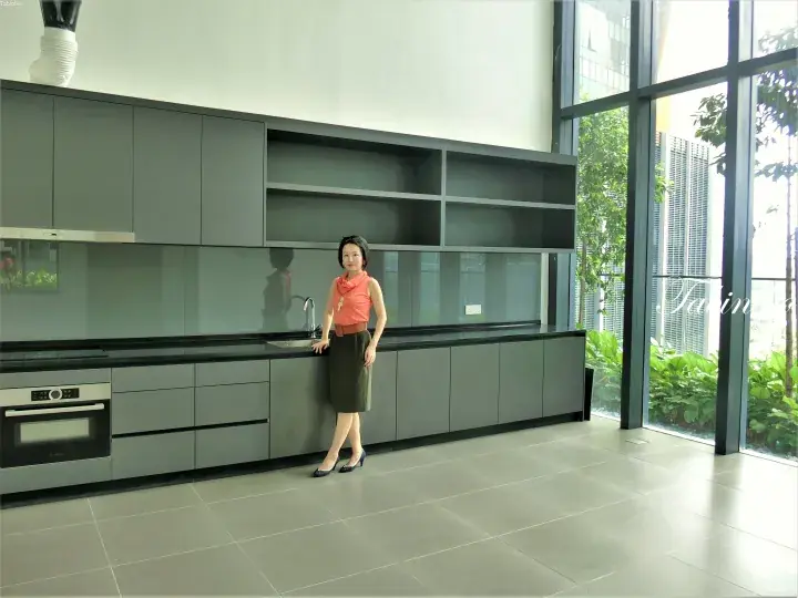 Woman posing in a modern grey kitchen with floor-to-ceiling windows overlooking greenery.