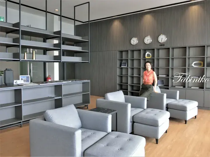 Modern office lounge with grey modular sofas, shelving units, and wall clocks in a contemporary workspace.