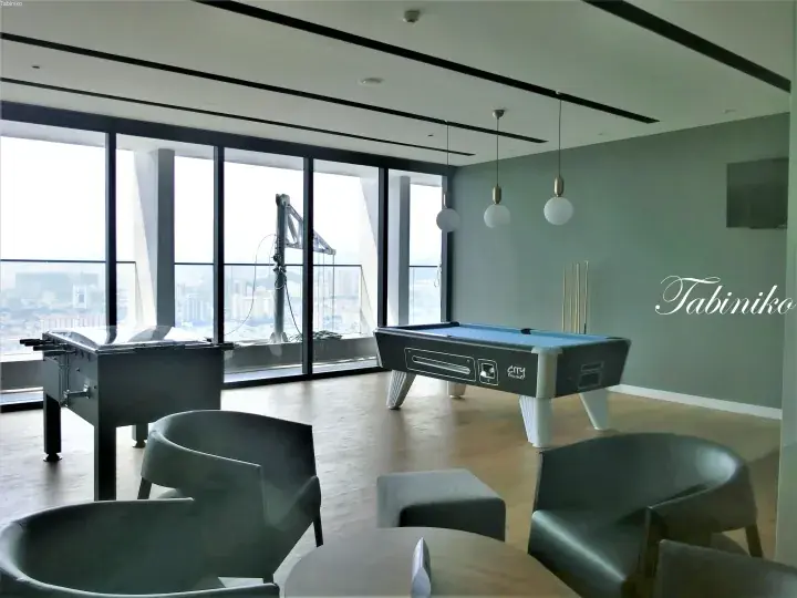 Modern recreation room with pool table and foosball near floor-to-ceiling windows overlooking a city skyline.