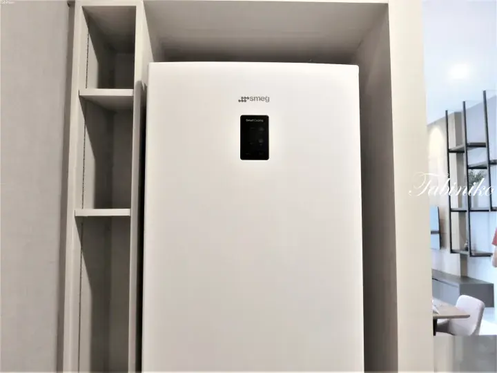 White Smeg smart refrigerator with digital display installed in a modern built-in cabinet.