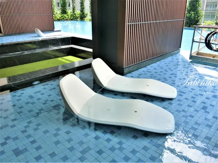 White lounge chairs on a blue tiled pool deck at a modern Malaysia property.