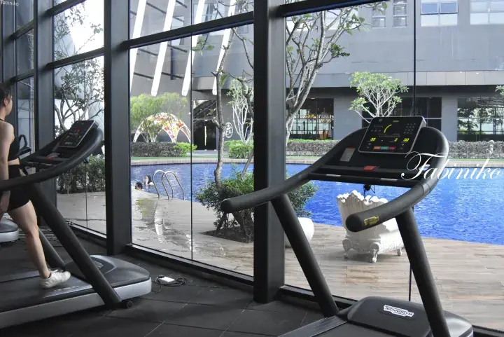 Woman running on a treadmill in a gym overlooking a swimming pool at a modern property.