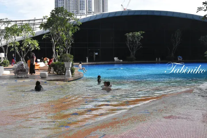 Guests enjoying the resort’s lagoon-style pool with shallow and deep sections, surrounded by tropical greenery and a modern building.