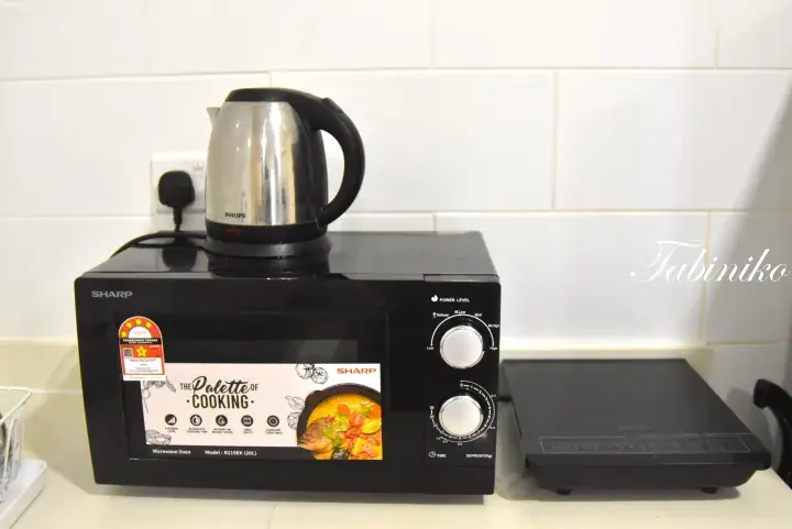 A black Sharp microwave oven with a kettle on top sits on a kitchen counter next to a portable induction cooktop.