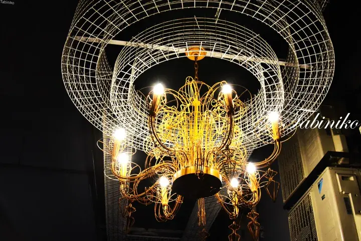 Modern chandelier with golden wire design and white mesh rings hanging in a dimly lit interior space.