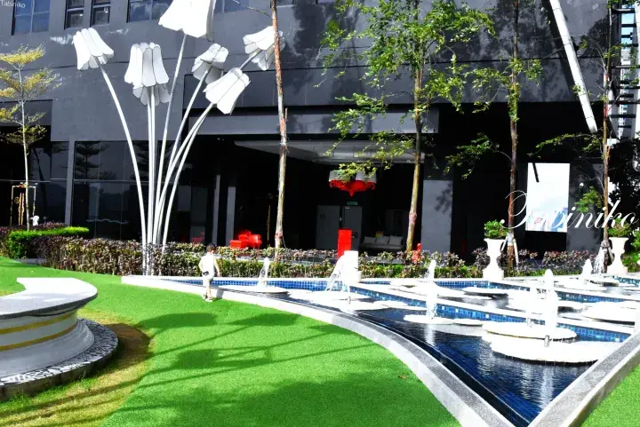 Modern building entrance with a decorative fountain and large white flower sculptures in a landscaped garden.