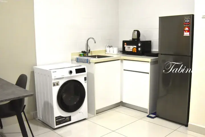 Compact kitchenette with a washing machine, sink, microwave, and refrigerator in a modern rental unit.