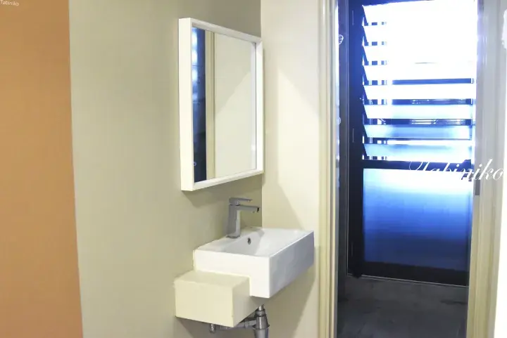 Modern white wall-mounted sink with chrome faucet and rectangular mirror in a bathroom with blue-tinted glass door.