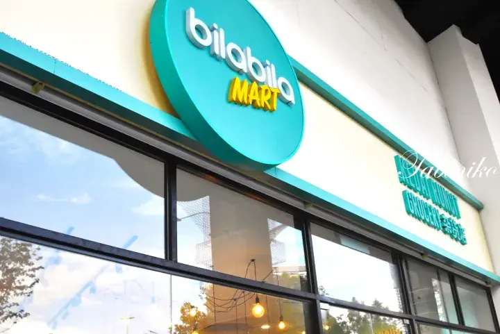 Exterior view of Bilabila Mart storefront featuring teal signage and large glass windows reflecting the sky.