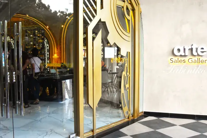 Entrance to Arte Sales Gallery at Tabinika, showcasing modern glass doors with gold accents and a marble floor.