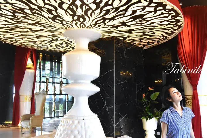 Woman admiring ornate ceiling and white pillar in luxurious hotel lobby with red curtains