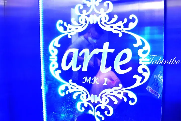 Blue neon sign displaying ‘arte MK I’ with decorative white filigree on a glass surface.