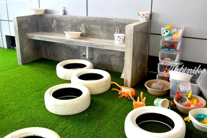 Children&rsquo;s play area with white tires and water play station on artificial grass.