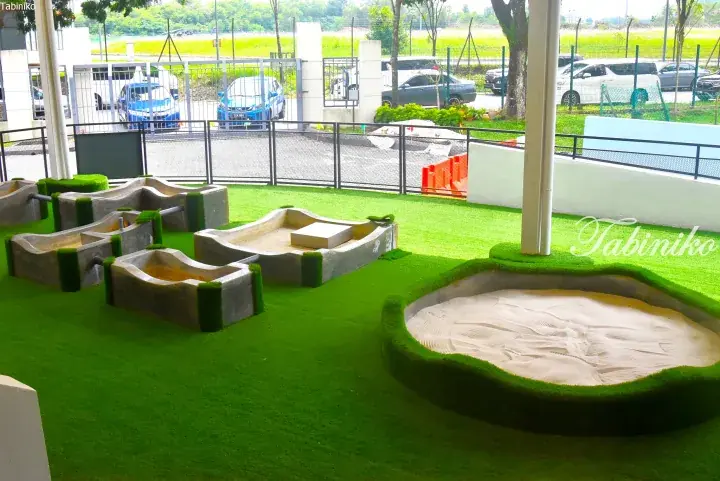 Children&rsquo;s play area with artificial grass, concrete sandboxes, and a large circular sand pit at a modern property.