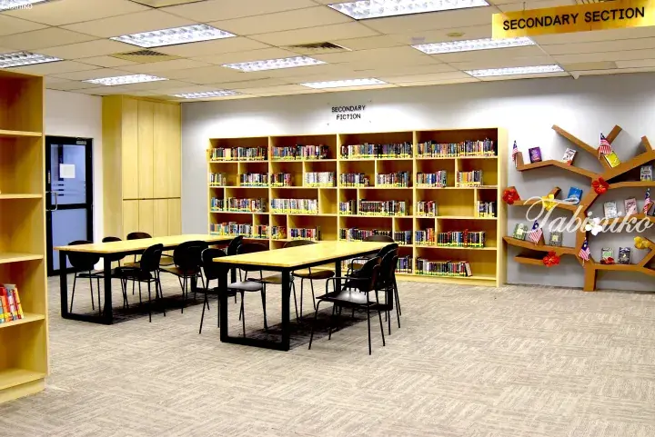 Spacious secondary section library with wooden bookshelves, study tables, and chairs in a modern educational facility.