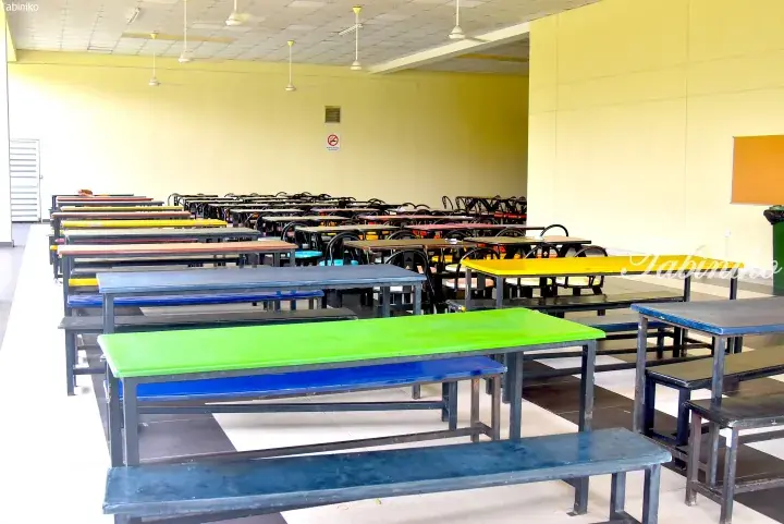 Rows of colorful tables and benches in a spacious, modern cafeteria with yellow walls and ceiling fans.