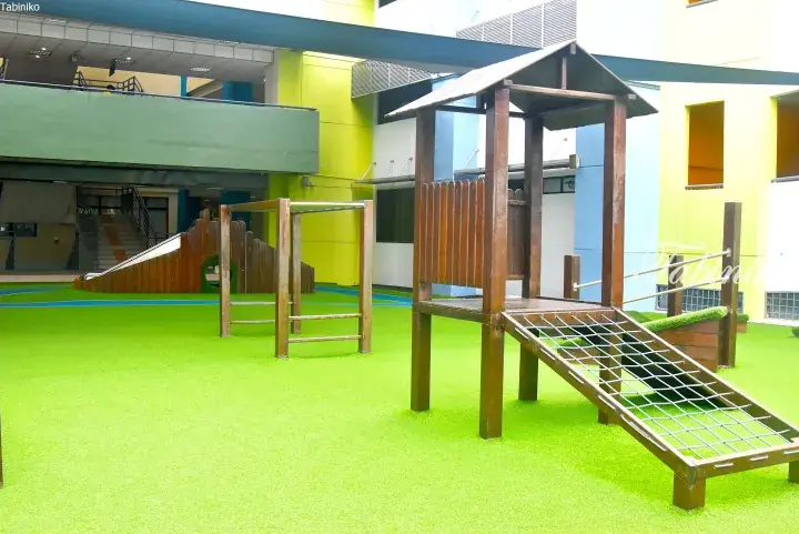 Outdoor playground with wooden play structures and green artificial turf at a modern property.