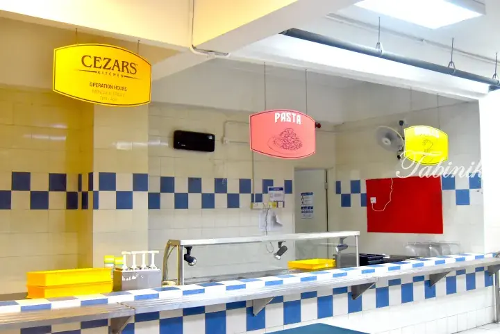 Cezar&rsquo;s Kitchen food stall interior with yellow signage, pasta sign, and blue-and-white tiled counter.