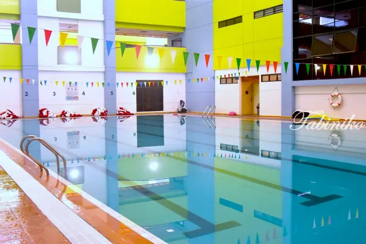 Indoor swimming pool with lane dividers, colorful bunting flags, and bright yellow walls.