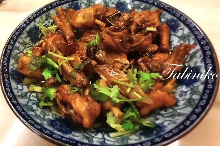 A bowl of savory braised chicken garnished with fresh cilantro, served in a traditional blue and white patterned dish.