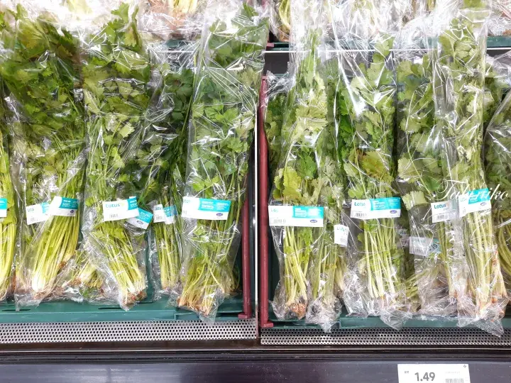 Fresh coriander bunches packaged in clear plastic bags displayed on a supermarket shelf with price tag.