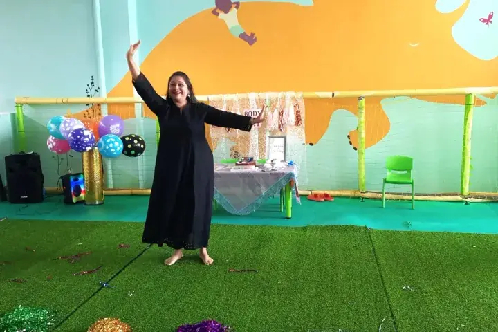 A woman in a black dress dancing at a children’s party with colorful balloons and a decorated play area.