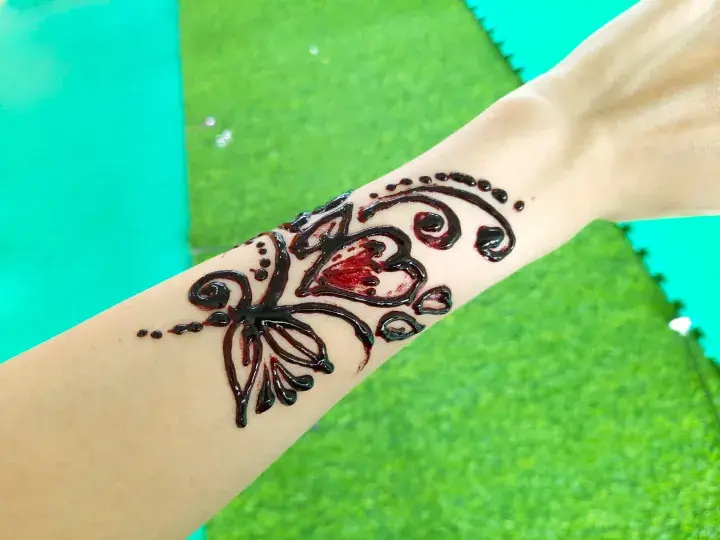 Fresh henna tattoo design on a person’s wrist against a green background.