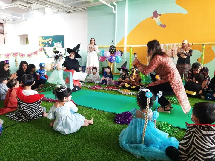 Children in costumes watch a storytelling performance at a colorful indoor play area.