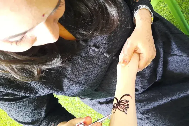 A woman applies intricate henna designs to a client’s wrist using a cone.