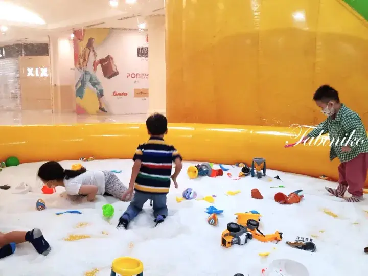 Children playing in a white sand pit with toys at a shopping mall in Malaysia.