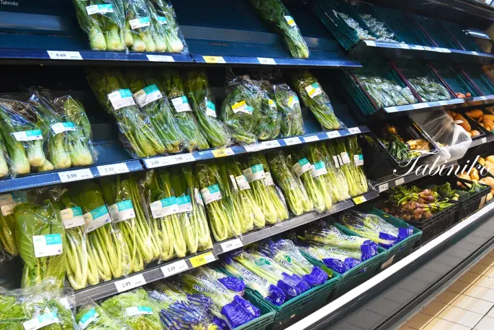 Fresh vegetables neatly arranged on supermarket shelves with price tags in a refrigerated display.