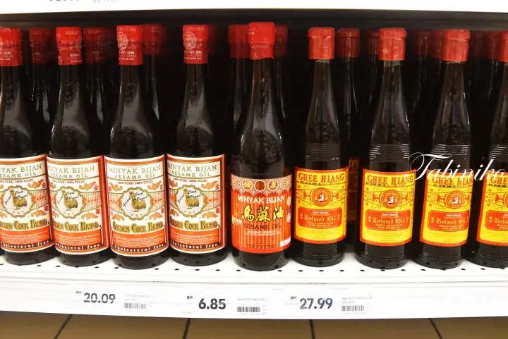 Shelves stocked with bottles of Ghee Hiang sesame oil and Minyak Bijan in a Malaysian grocery store.