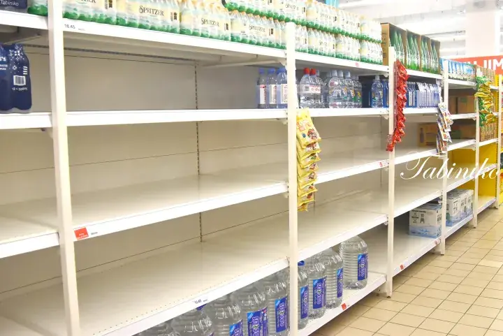 Empty supermarket shelves with only a few water bottles remaining on the top and bottom racks.